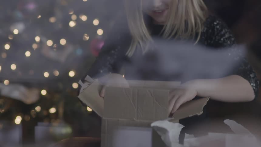 A girl opens a box near a christmas tree