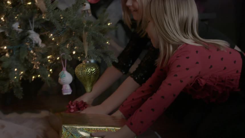 Two girls place presents under a christmas tree