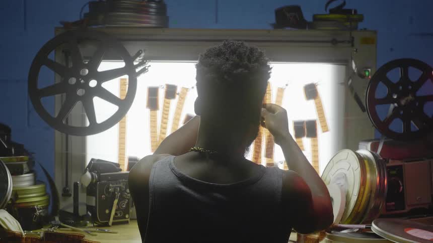 Man looking through a strip of brown film reel in a developing studio