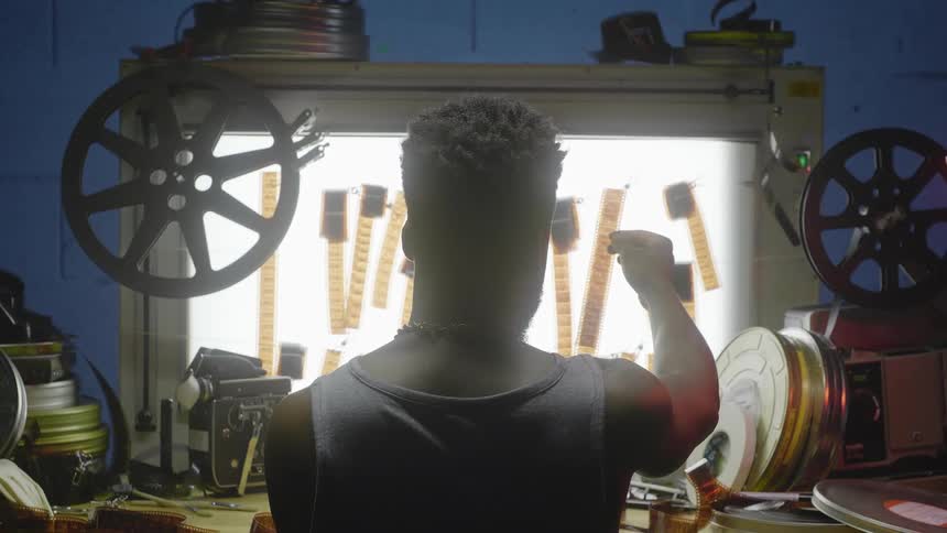 Man sitting in front of a light display with undeveloped film reels posted to it while he observes one