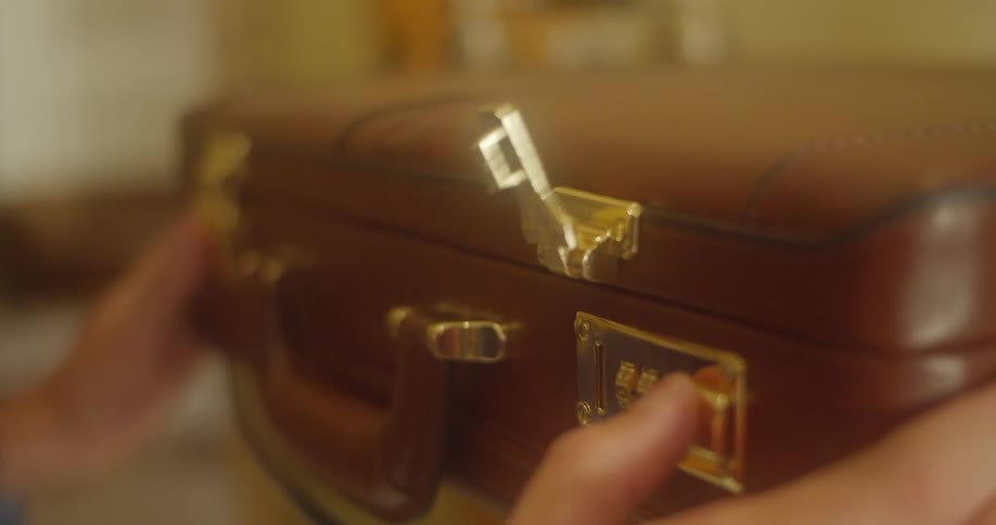 Close up of hands opening the combination locks of a leather briefcase