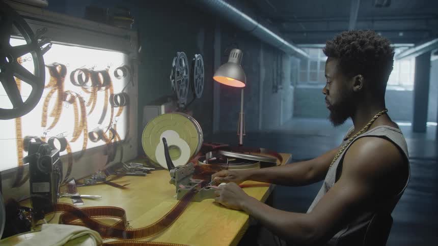 A filmmaker sits at his desk and cuts off pieces from a film reel