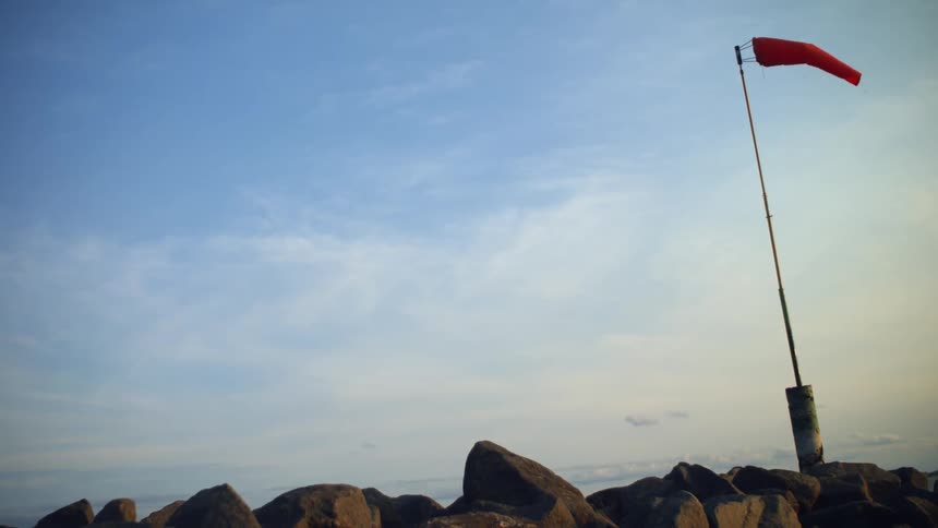 A red flag is on a pole sitting on rocks against a blue sky