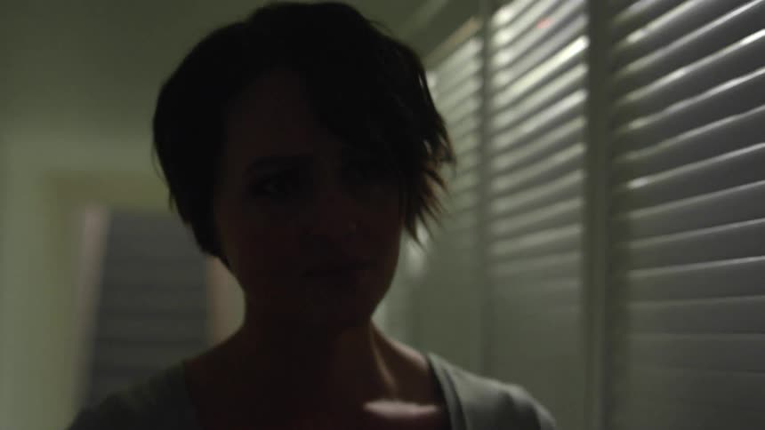 A young woman walks through a house with a look of apprehension on her face
