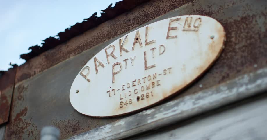 An oval shaped white sign covered in rust with writing
