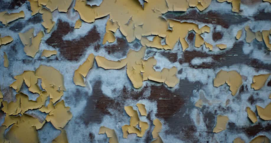 A wall with flaking paint and white and brown spray paint