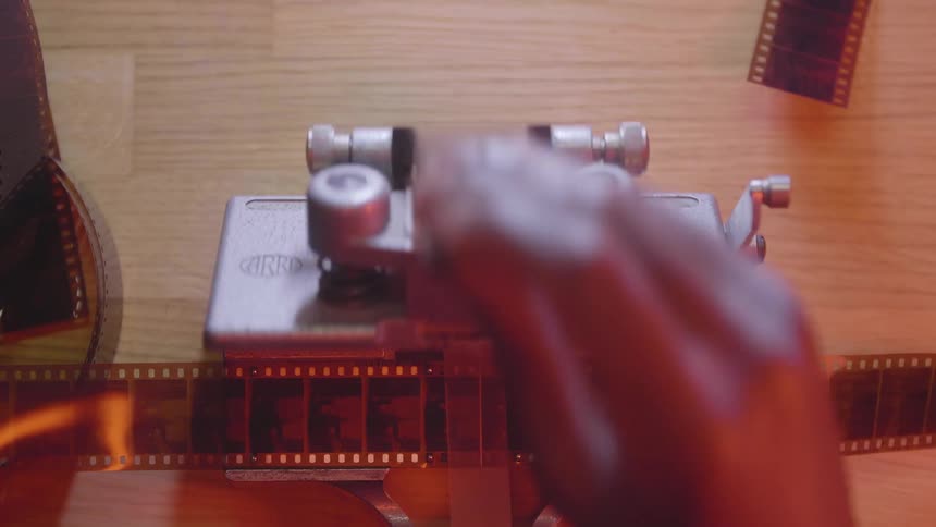 Man uses a film splicer to tape together a strip of film