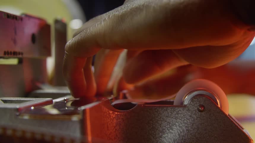 Man uses a vintage film splicer to cut a strip of film