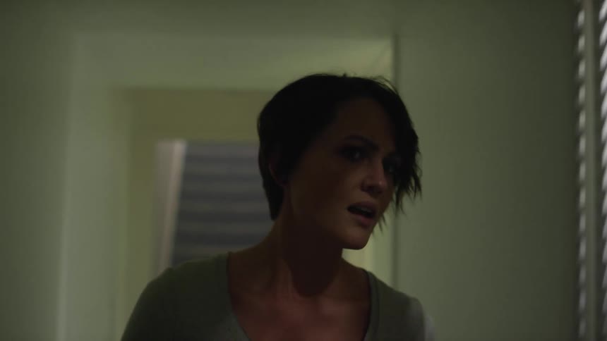 A fearful woman slowly walks through a corridor in a house during the day
