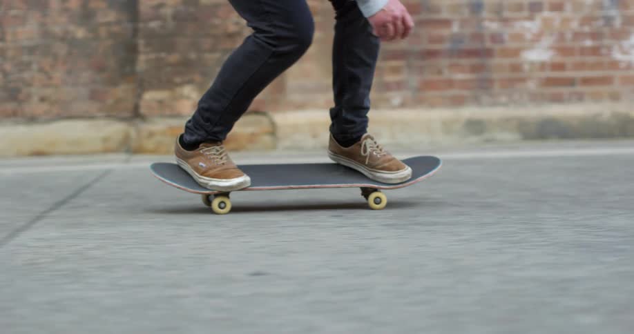 A skateboarder rides on pavement in front of brick buildings while doing a trick with the board during the day