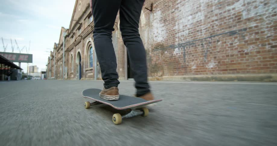 A person rides on a skateboard down pavement in front of red brick buildings during the day