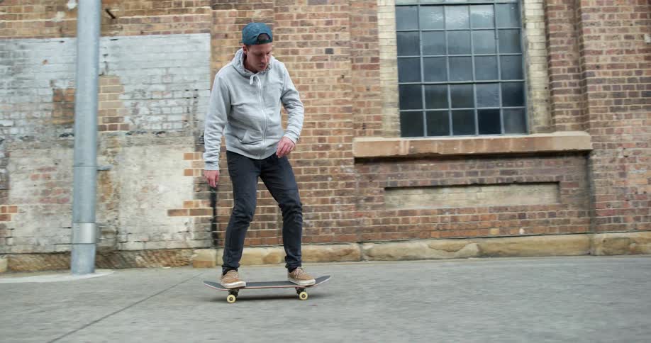 A man rides a skateboard on a sidewalk and does a trick with the board during the day outside