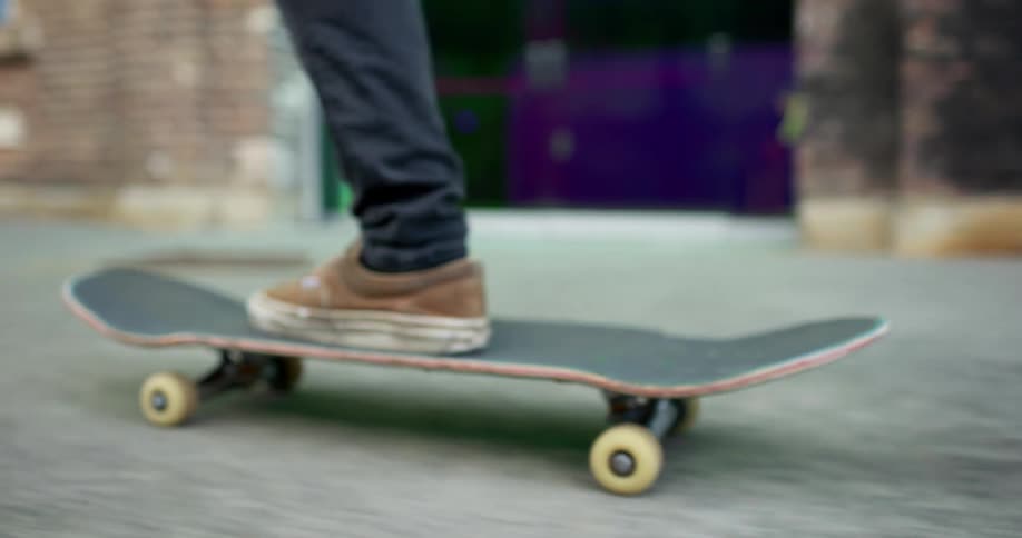A teenager rides a skateboard down a city sidewalk past brick buildings