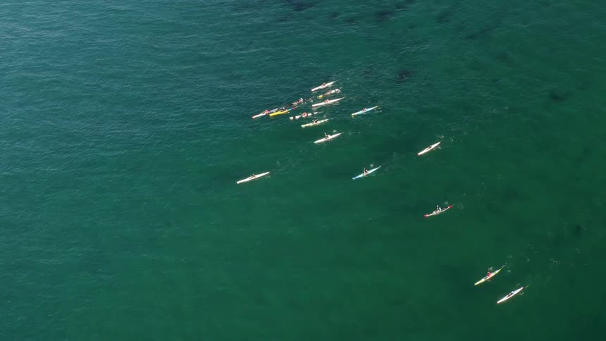 Group of people rowing on kayaks over the green clear ocean waters