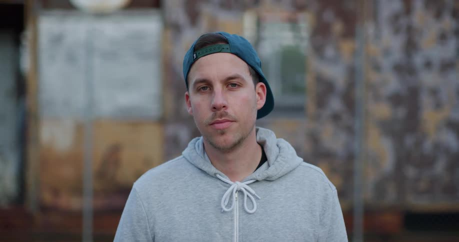 Young man wearing a baseball hat and a hoodie looking at the camera