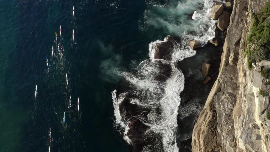 Kayakers paddle in the ocean below a tall cliff