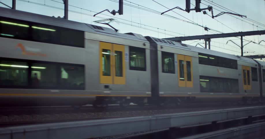 A passenger train passes by with people sitting on the upper and lower decks of train cars