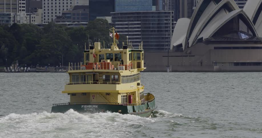 A yellow and green ferry moves through the water with a view of a city and buildings during the day