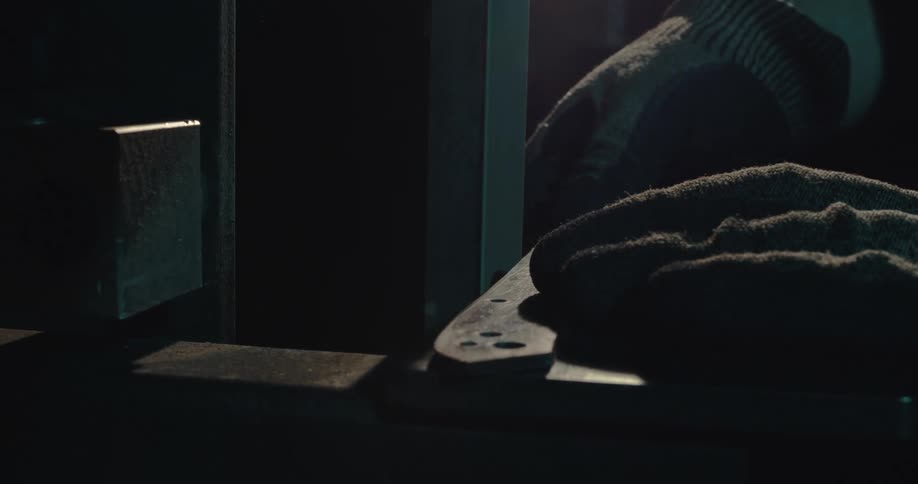 Hands wearing black work gloves sharpening a tool on a machine