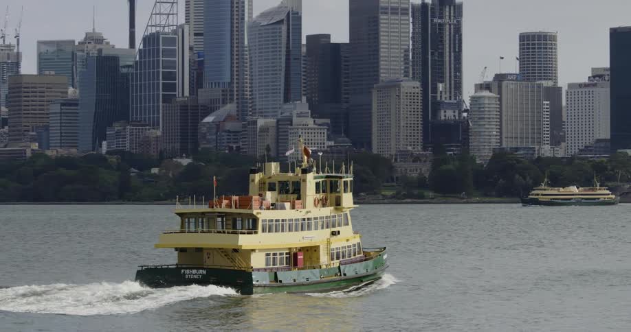 A ferry drives on the water with a city view behind it