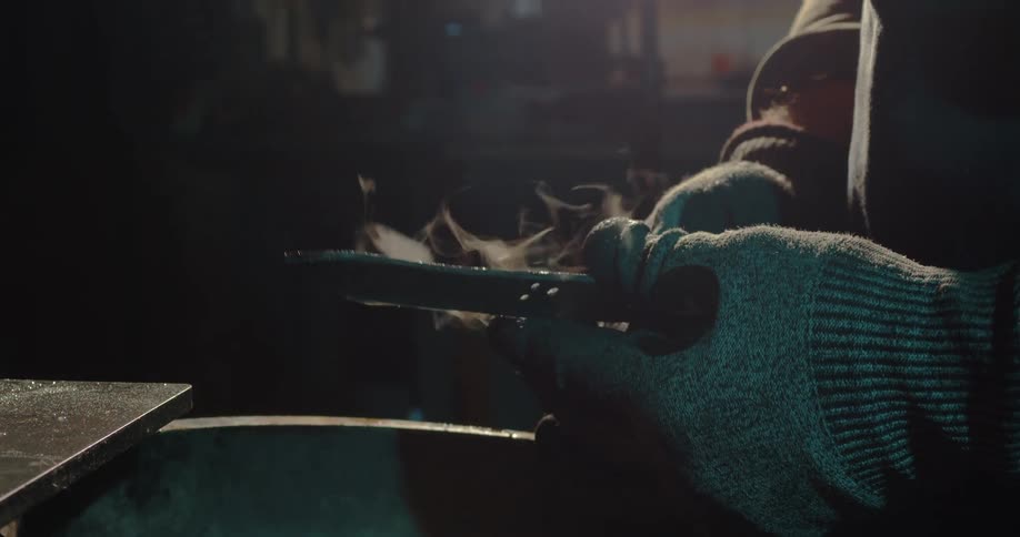 A person picks up a knife with steam and droplets of water coming off of it