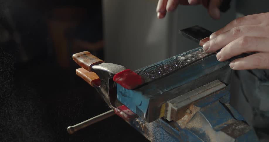 Man sprays a knife to wet it before sharpening it over a vice