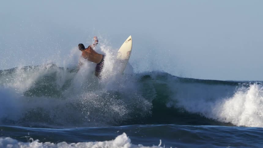 A surfer riding a wave atop a surfboard makes a sharp turn to pass over the top of the wave