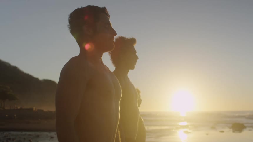 Three men standing on a beach with the sunset the ocean the sky and clouds in the background