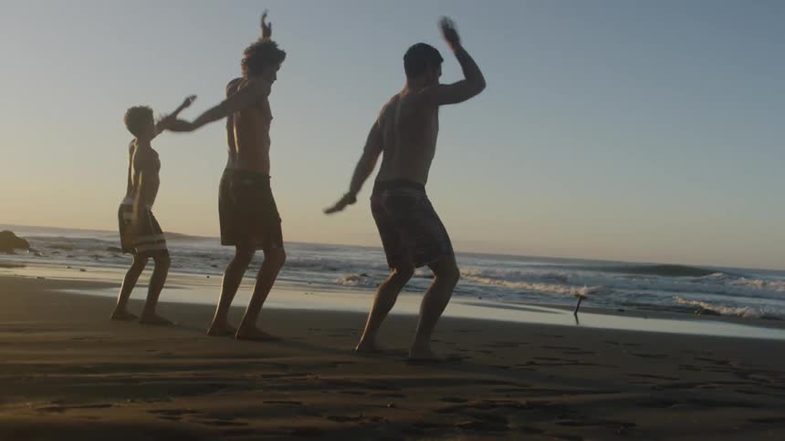A young boy and two men stand on the shore and swing their arms back and forth