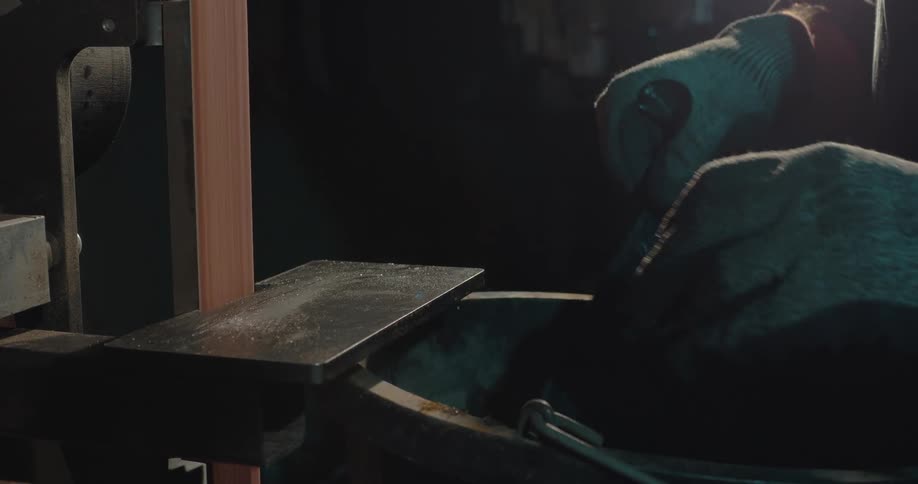 A forging a knife uses a power tool to sand one of the edges in a workshop