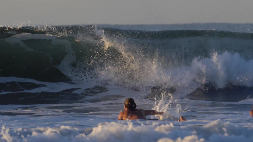 A large ocean wave crashes as it rolls toward a pair of swimmers