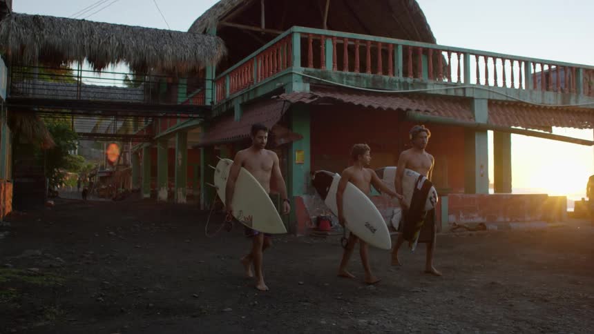 Trio of surfers coming out of a building with surfboards at morning