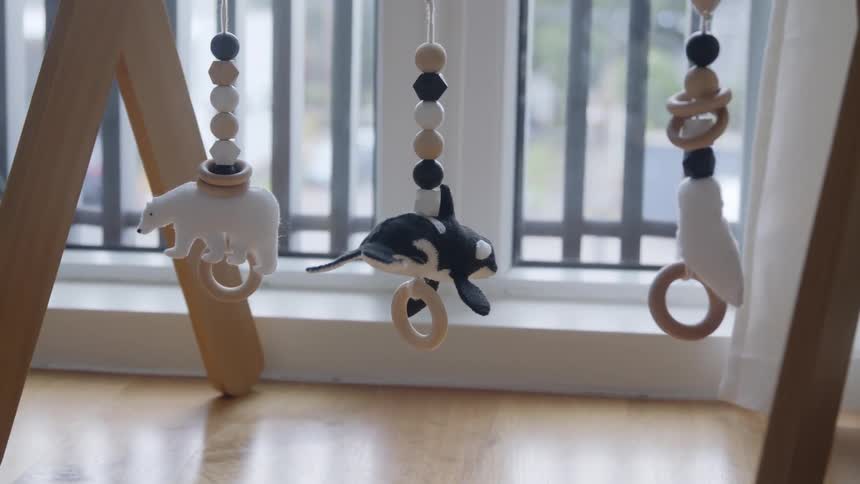 A baby mobile with a window with blinds and bars and trees in the background