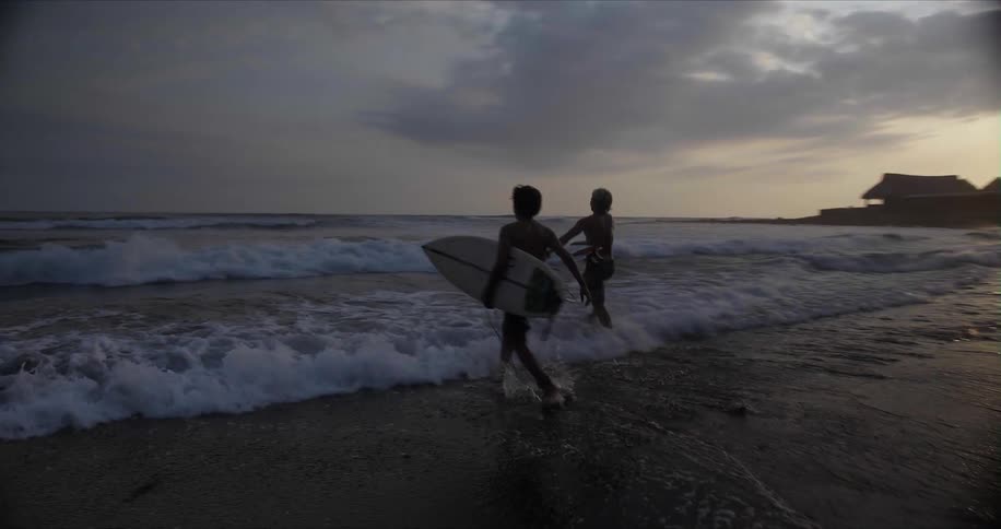 Two young surfers running to the ocean with surfboards at sunset