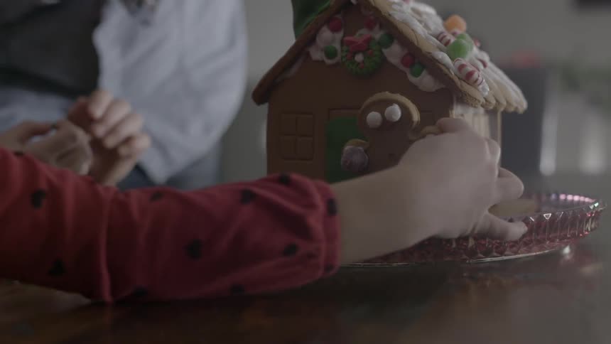 Two young girls decorate a gingerbread house