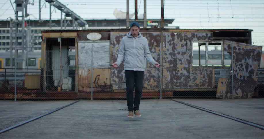 A man jumps rope working out outdoors as a train passes behind him