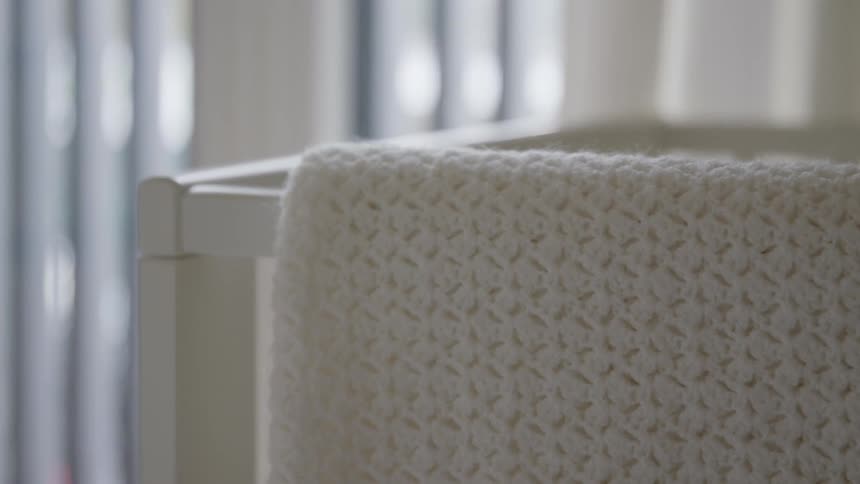 White blanket hangin over the edge of a crib in a baby room at home