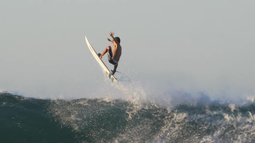 A wave knocks a teenager off his surfboard