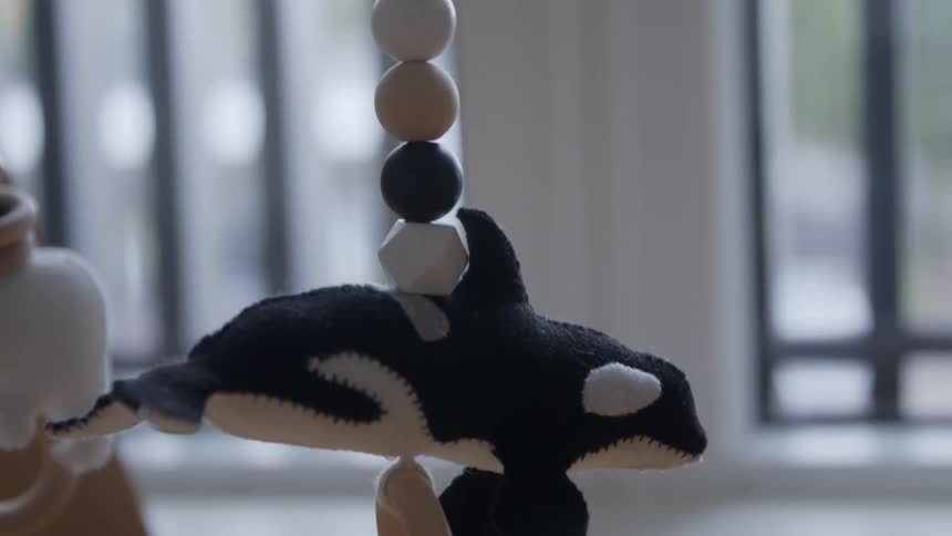 Stuffed orca plush toy hanging from a strand over a cradle at home
