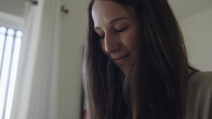A relaxed long haired woman smiles contently inside a room at home