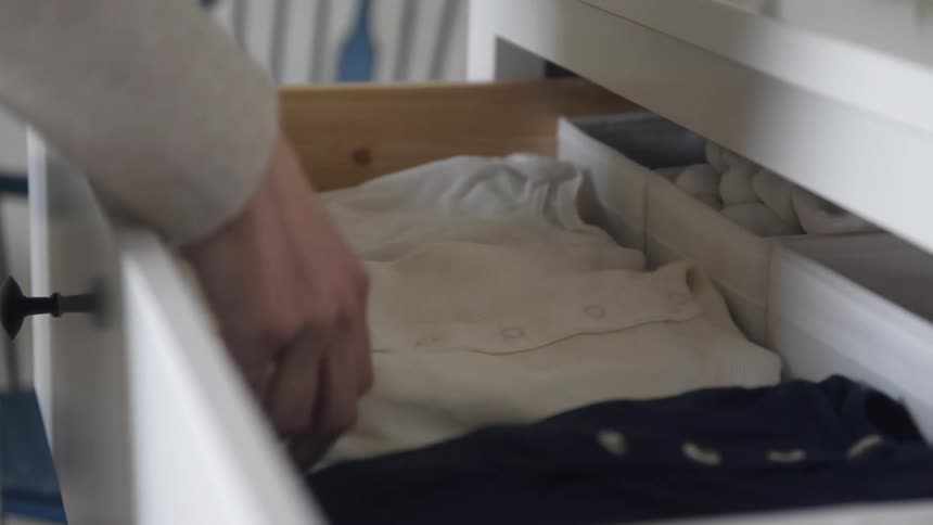A person folds onesies while putting them in a drawer