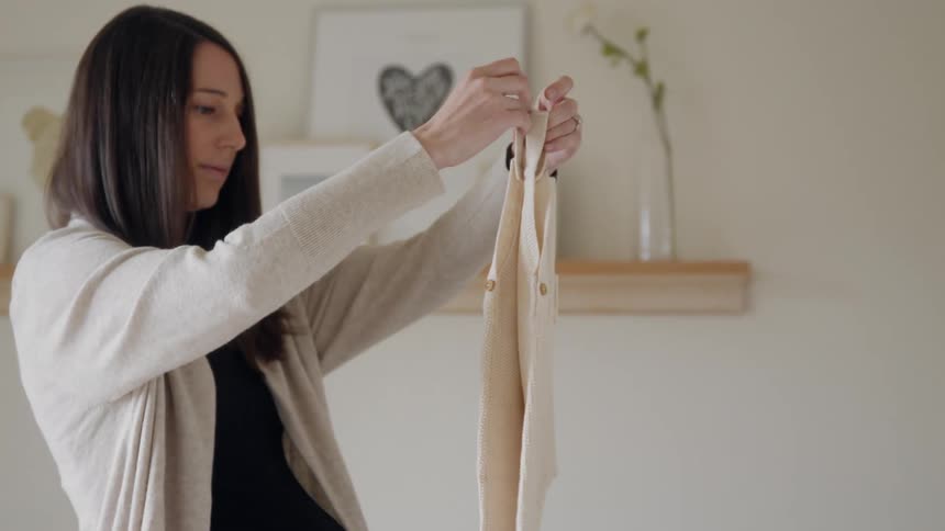 Woman in a nursery in folding baby clothes into a white dresser