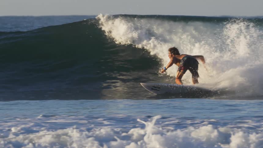 Male surfer rides a wave and performs maneuvers on a skateboard
