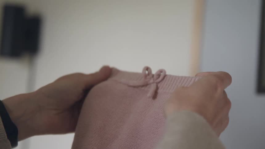 Womans hands folding a small pair of pink baby bottoms inside of a room