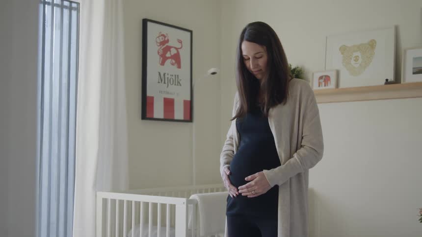 Young pregnant woman standing next to crib rubbing her belly