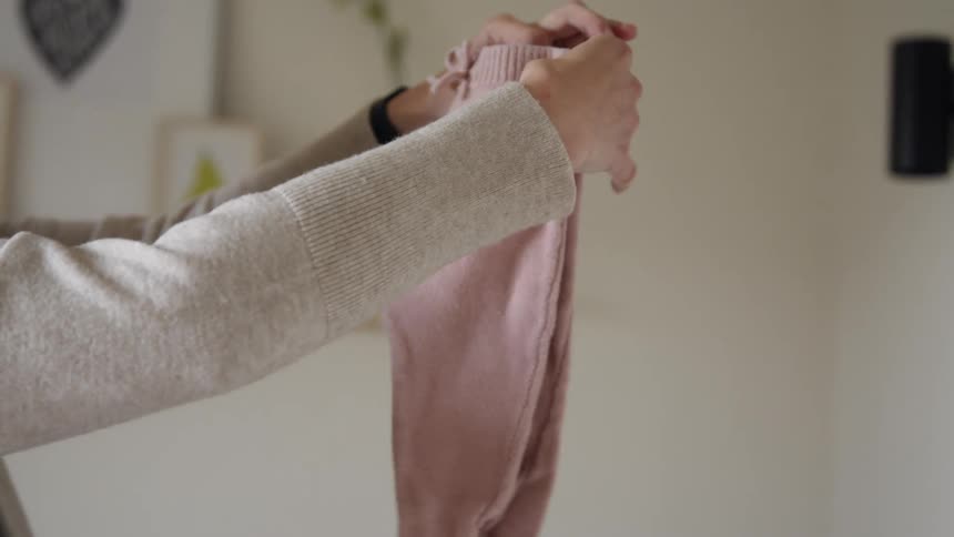 A pregnant woman lies baby clothing from the top of a dresser before folding it and putting it in a drawer
