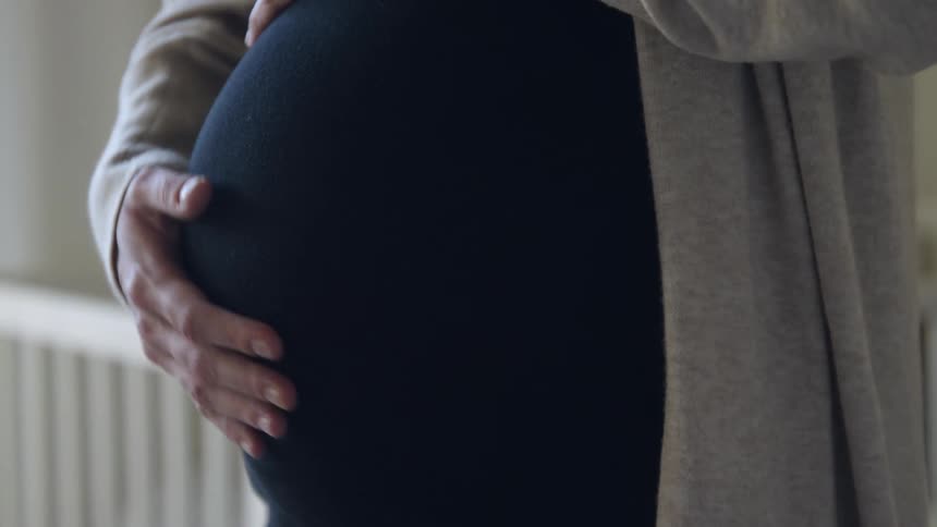 A pregnant woman caresses her belly while standing indoors during the day