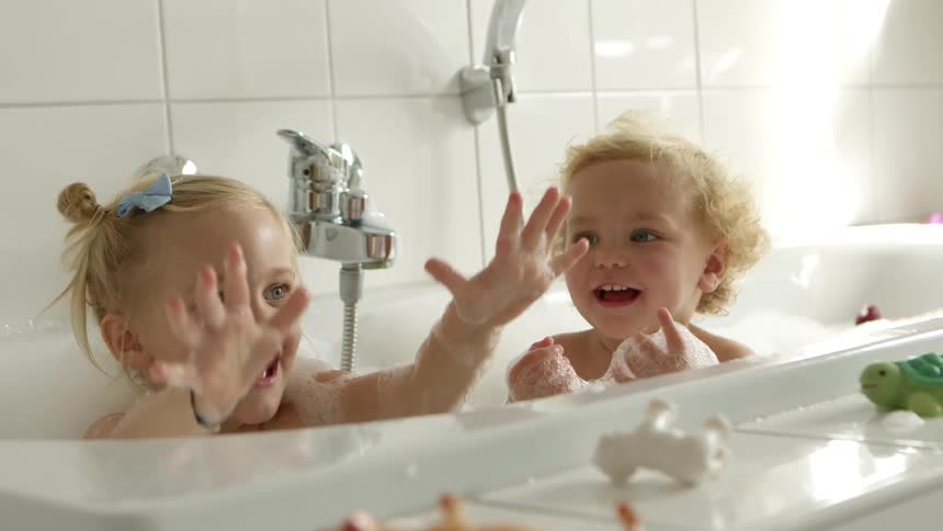 A young girl and her toddler brother smile as they play in a bubble bath