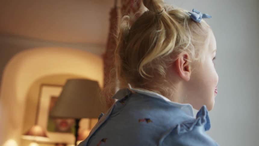 Small blonde girl sitting in a room with her toys stands up to look out the window