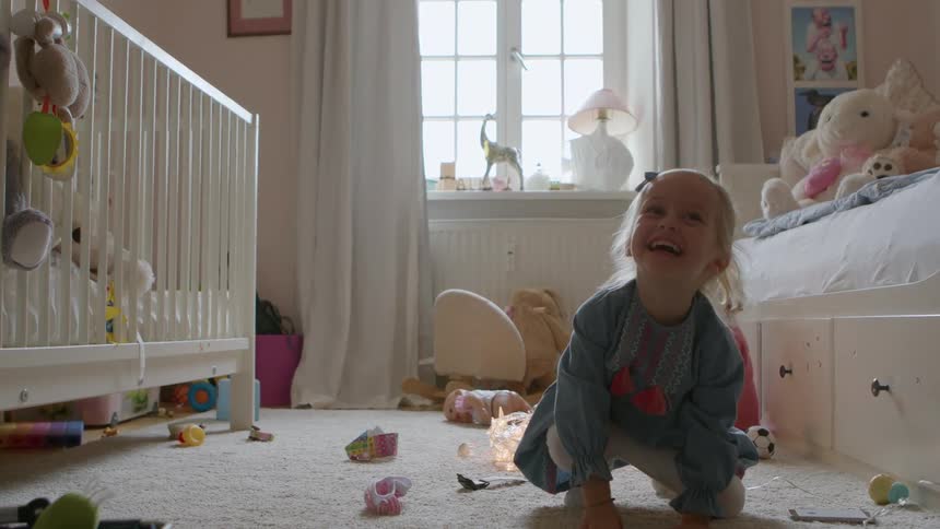 Two young toddler girls play in their room one making a big jump and falling to the floor